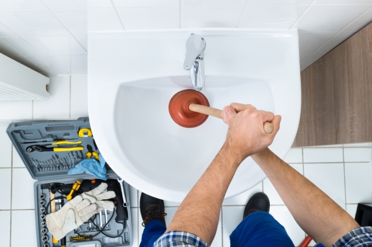 Male Plumber Using Plunger In Bathroom Sink